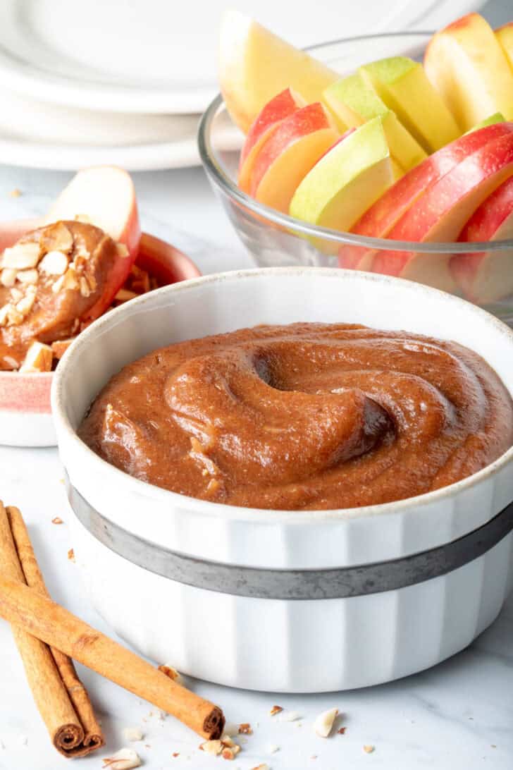 A white bowl filled with a Medjool date sauce. A clear glass bowl filled with fruit sits next to the bowl.