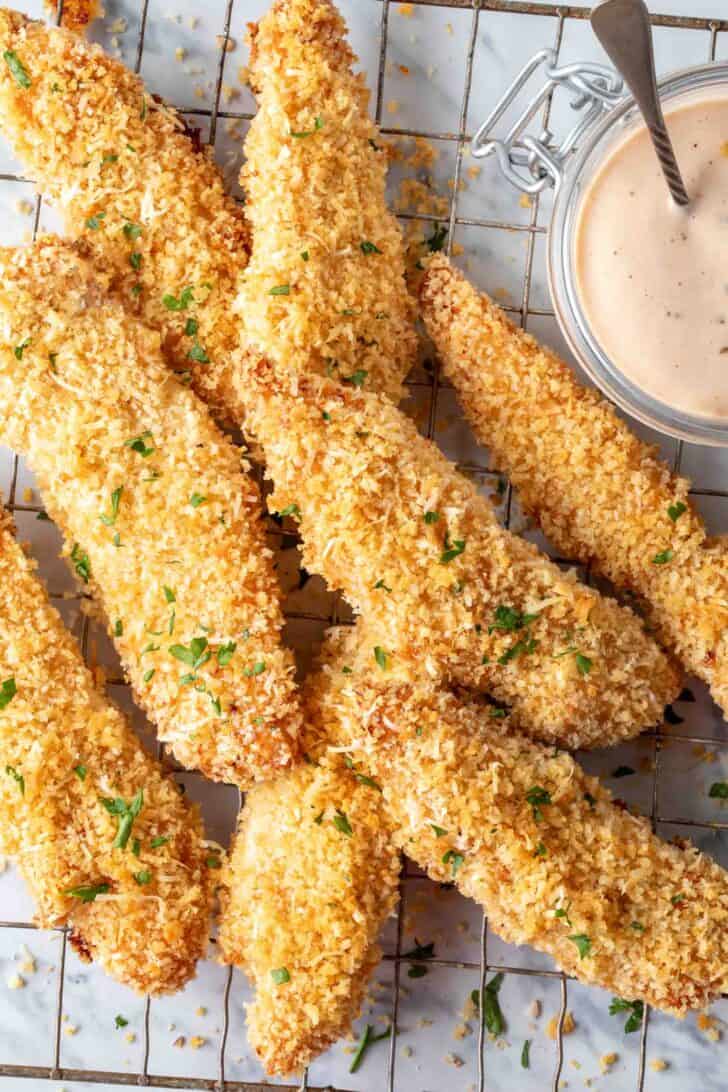 Cooked strips of breaded poultry on a wire cooling rack.