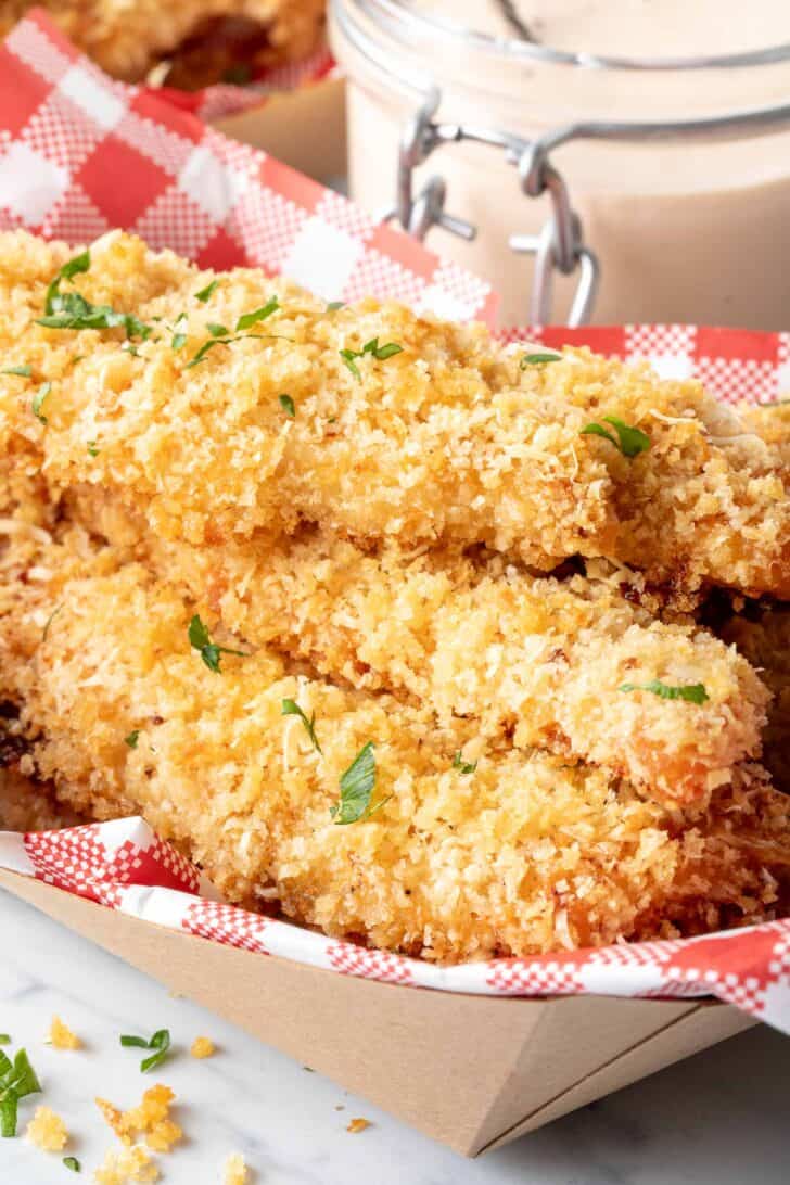 A paper deli container filled with oven baked chicken tenders.