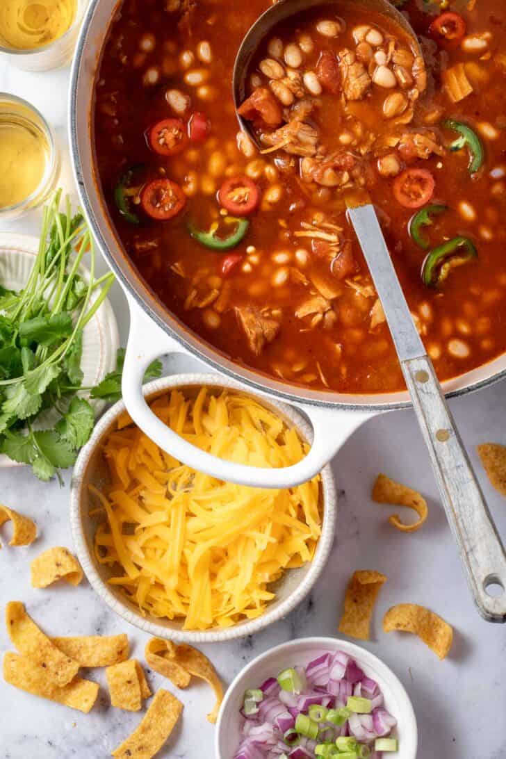 A white pot filled with turkey white bean chili. A ladle rests in the pot.