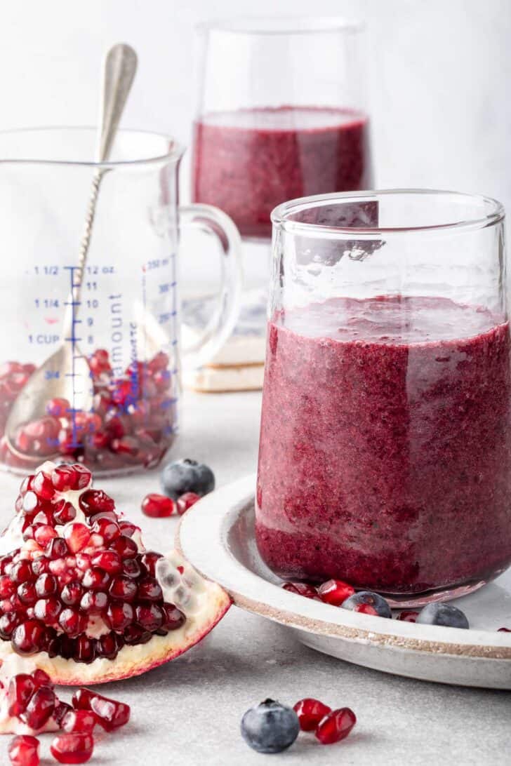 Two clear glasses filled with blueberry pomegranate smoothie.