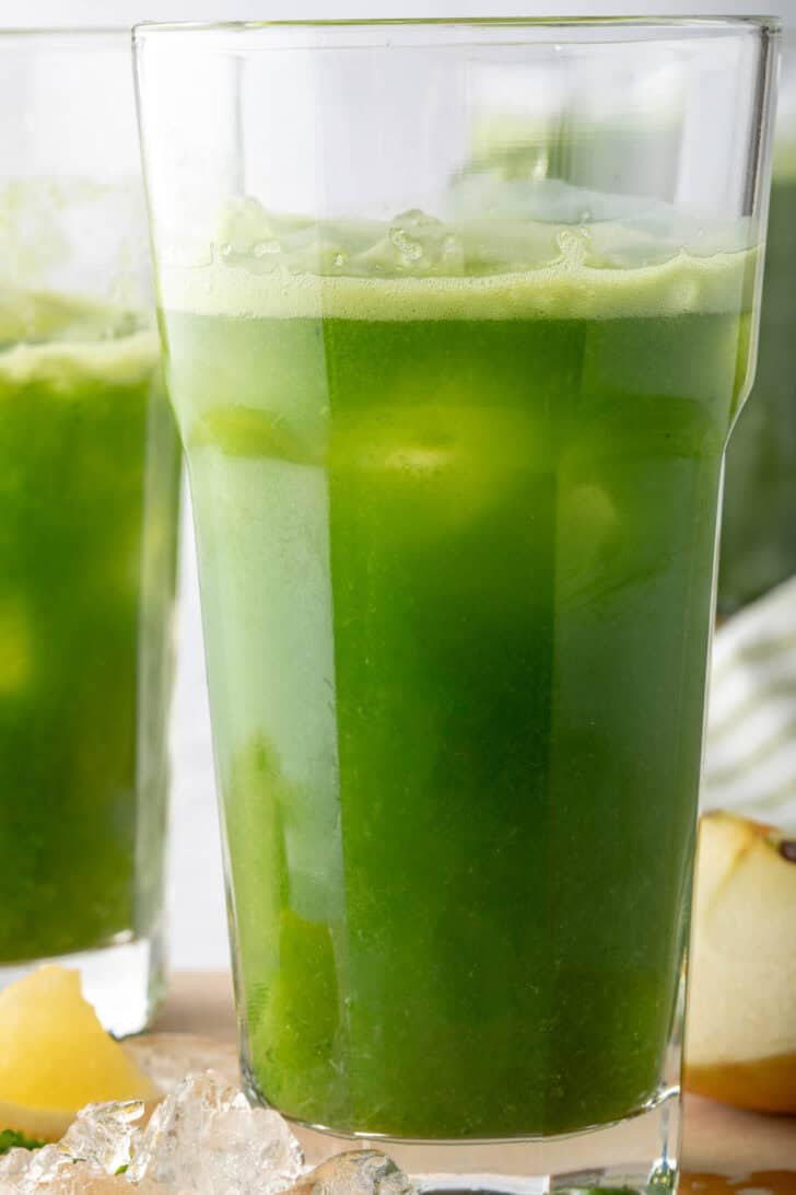 Two clear glasses filled with healthy green juice over ice.