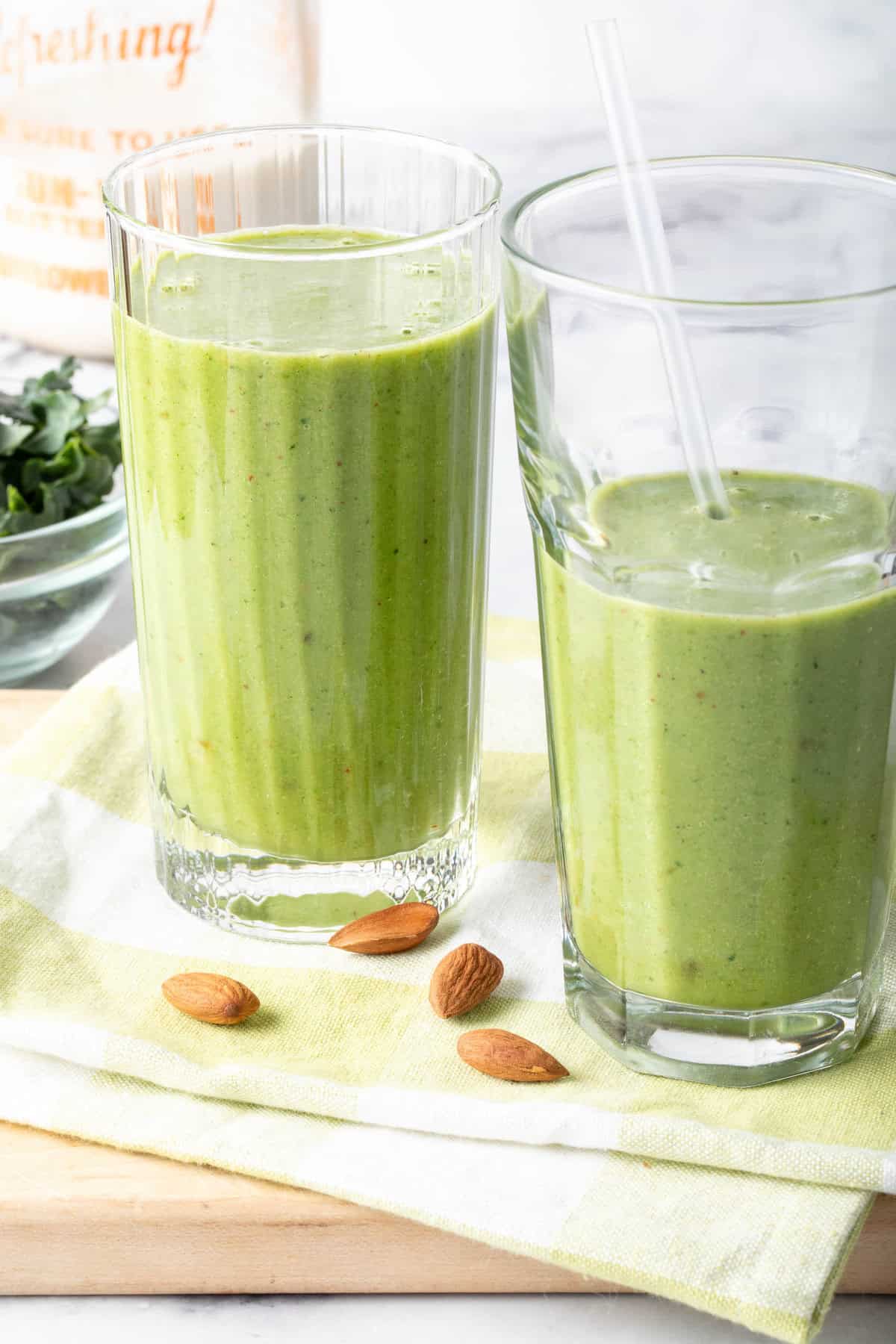 Two clear drinking glasses filled with kale fruit smoothie.