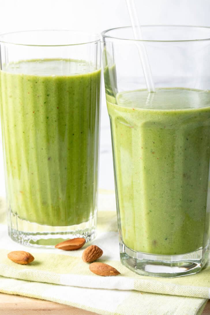 Two clear drinking glasses filled with kale smoothie.