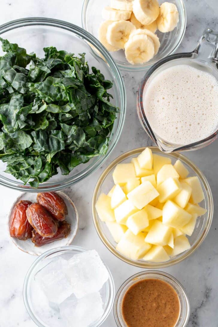 Clear glass bowls filled with chopped fruit, dates, almond butter and oat milk.