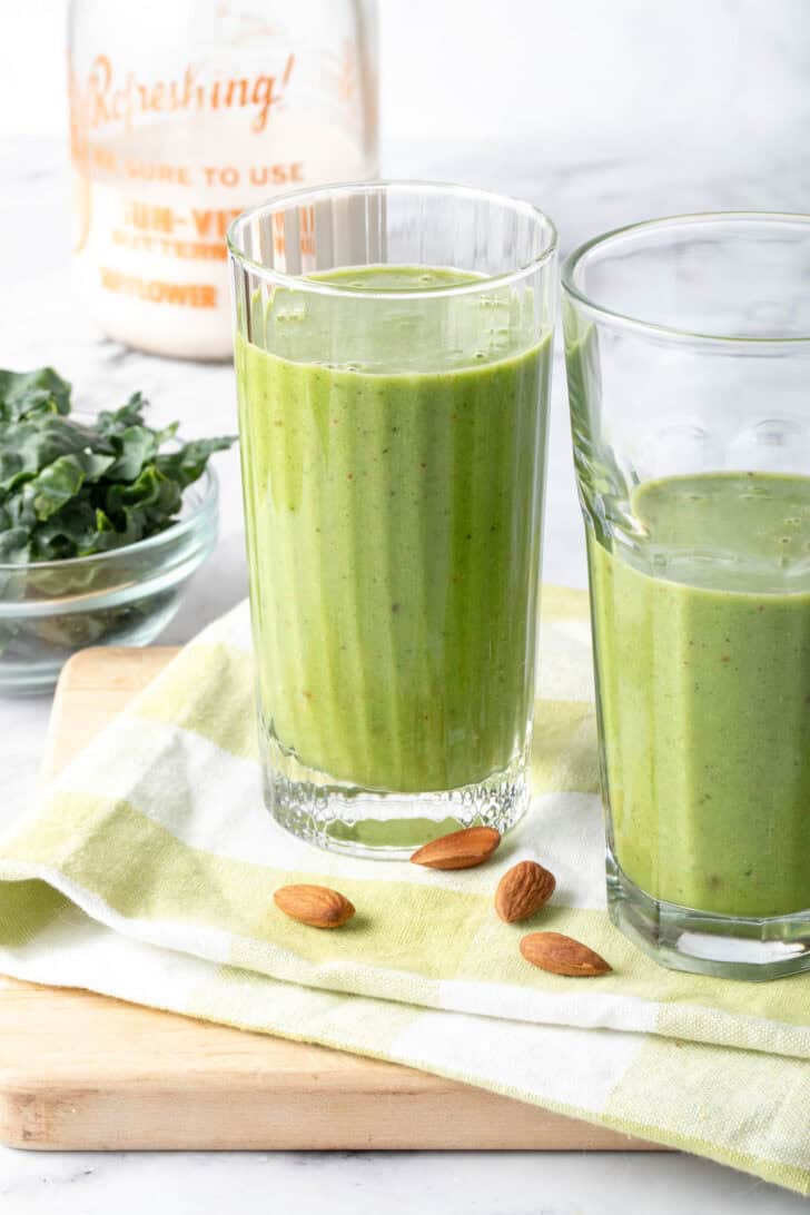 Two clear drinking glasses filled with kale fruit smoothie.