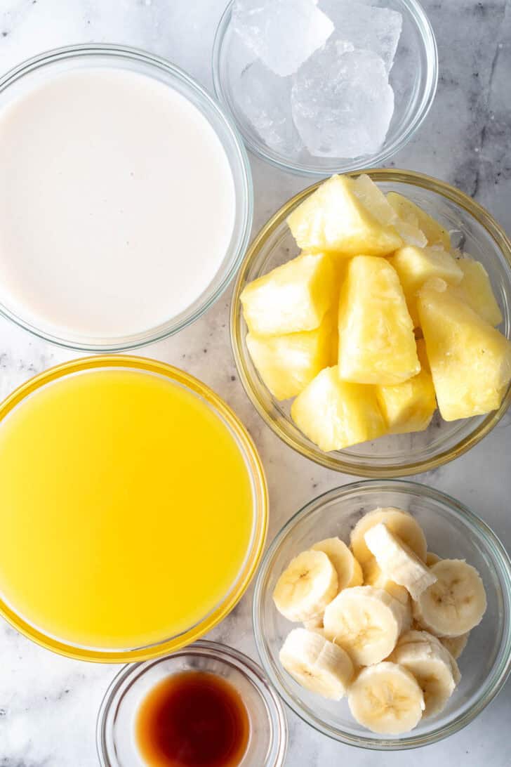 Clear glass bowls filled with oat milk, orange juice, chopped fruit and pure vanilla extract.