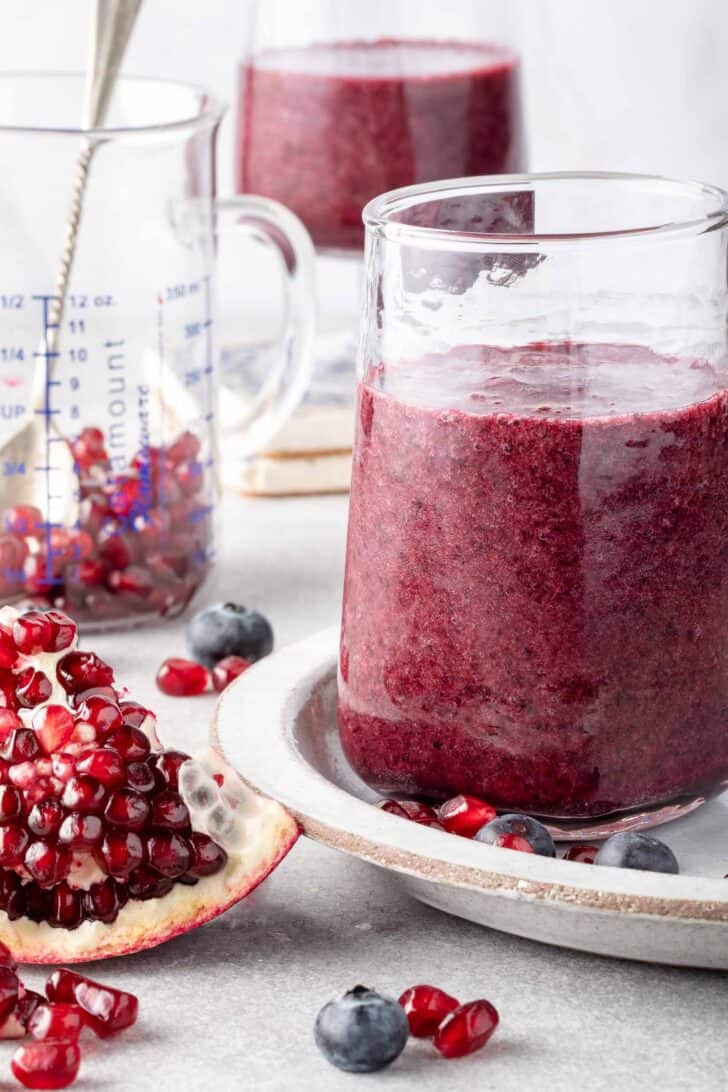 Two clear drinking glasses filled with pomegranate juice smoothie.