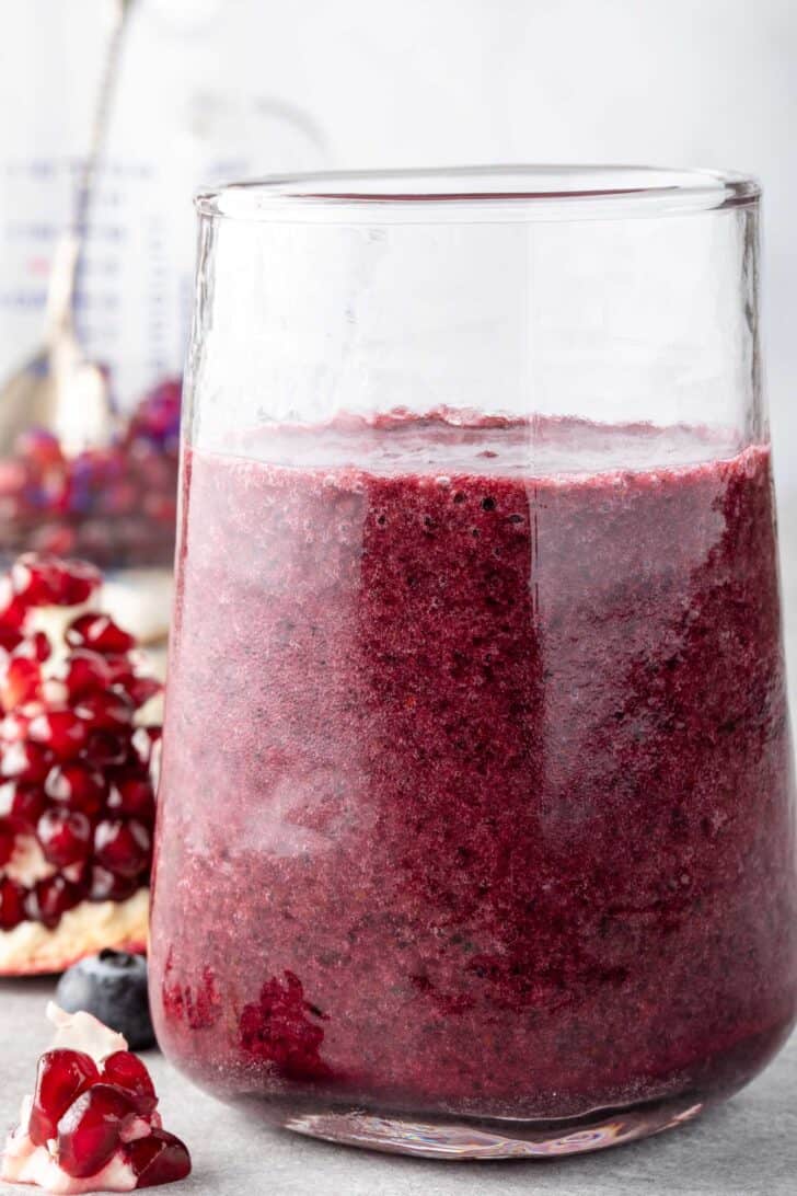 A clear drinking glass filled with blueberry pomegranate smoothie.