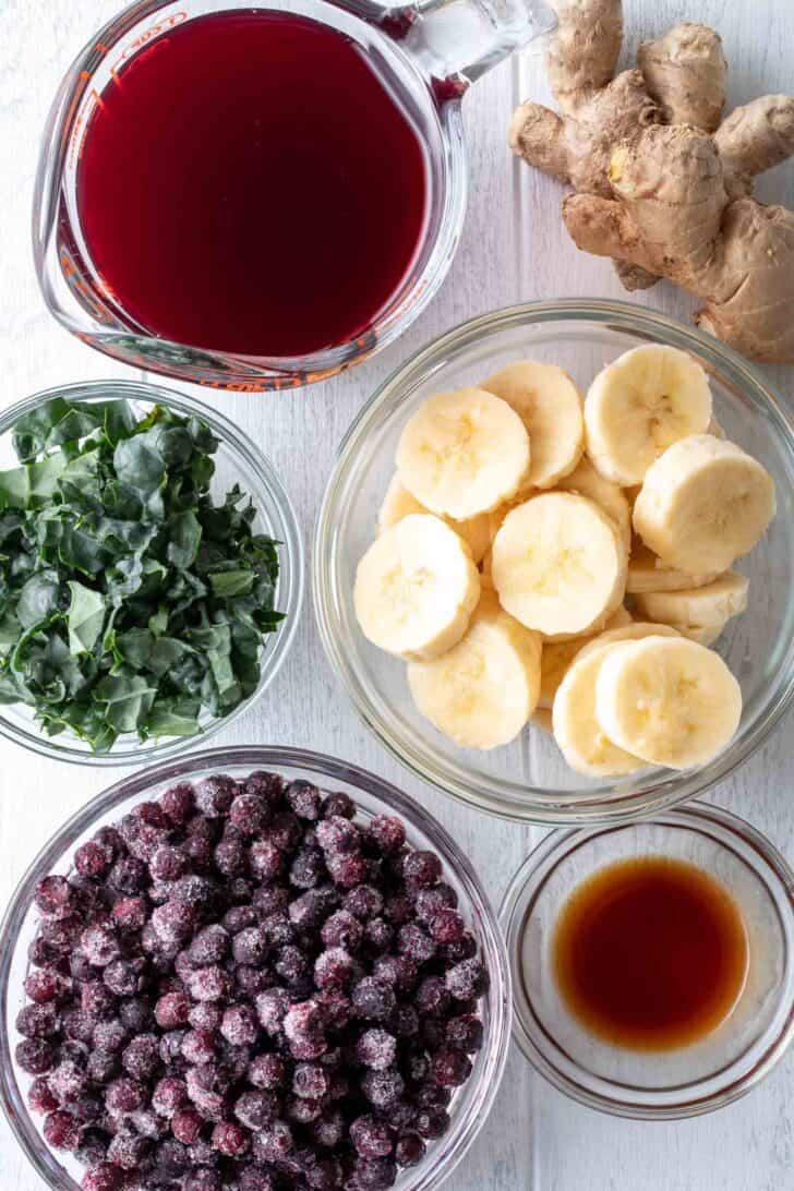 Clear glass bowls filled with frozen fruit, juice and chopped kale.