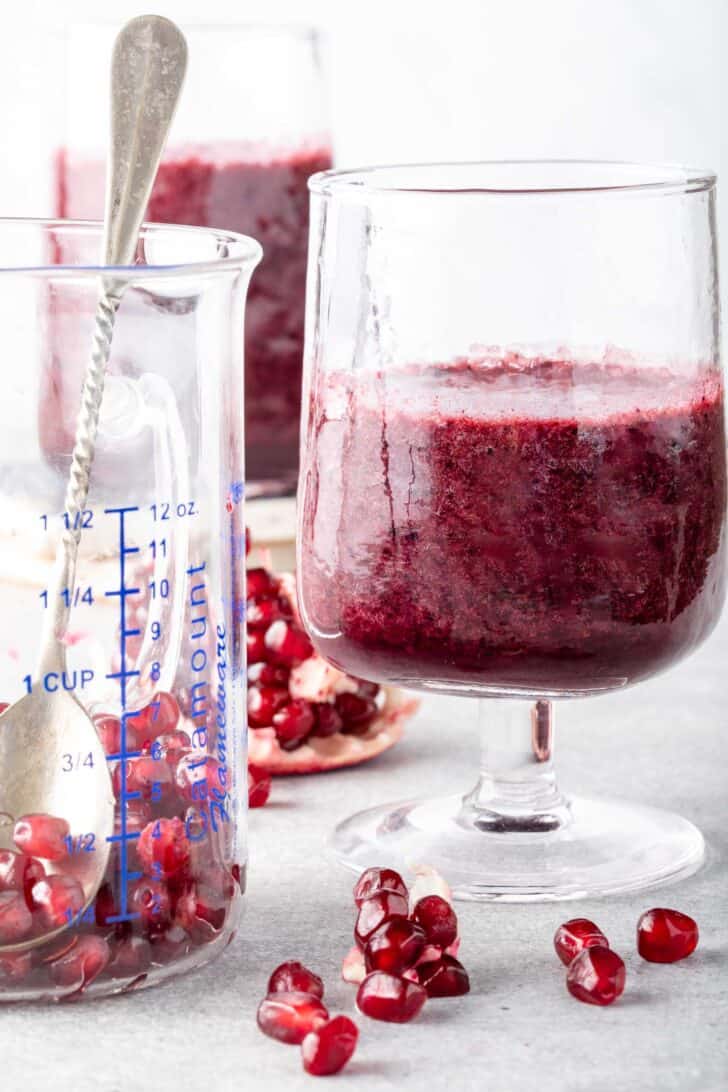 Two clear drinking glasses filled with pomegranate smoothies.