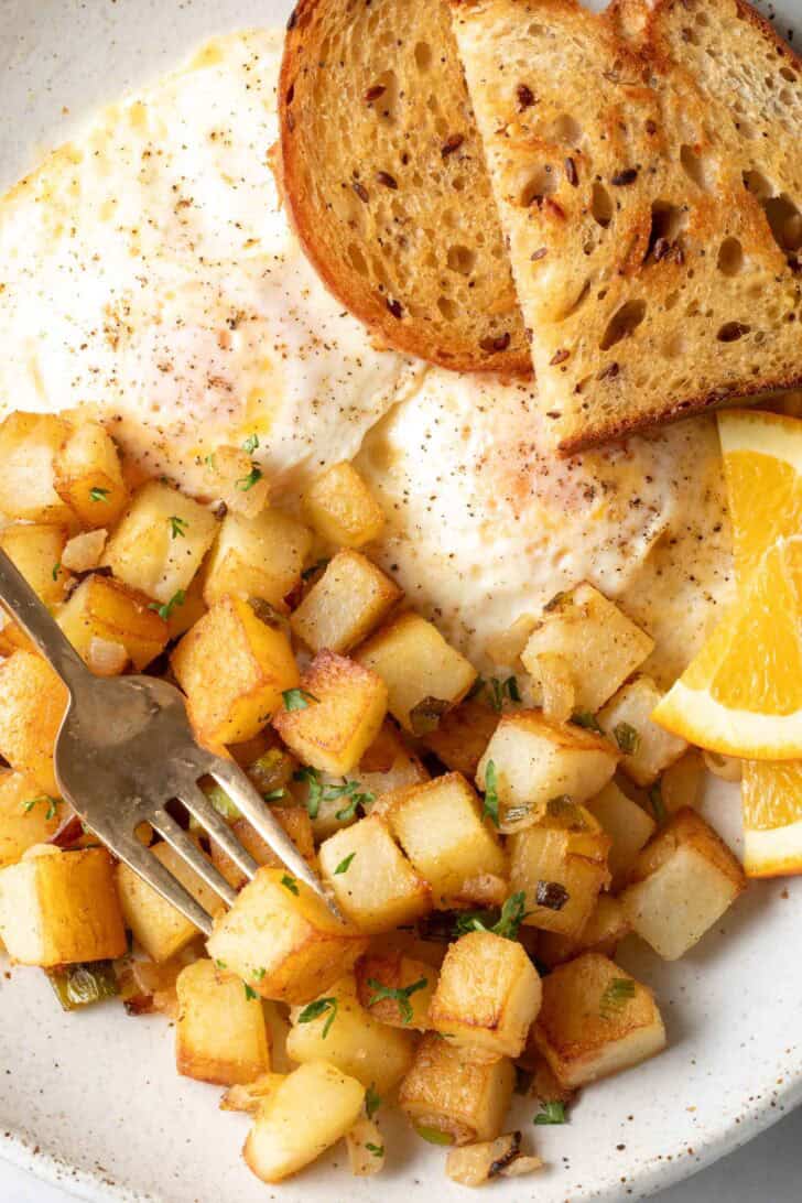 A white plate filled with fried eggs, toast and crispy breakfast potatoes.