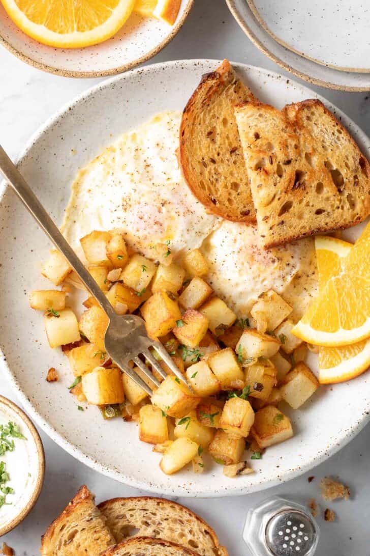 A white plate filled with fried eggs, toast and skillet breakfast potatoes.