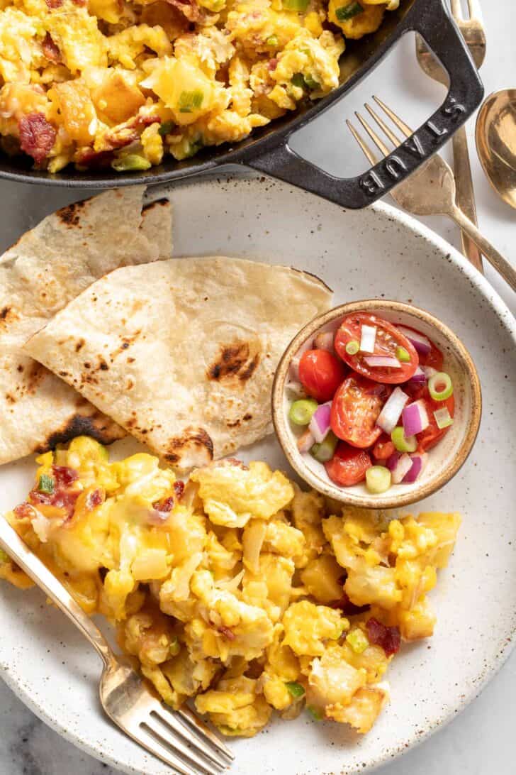 A plate filled with breakfast scramble with potatoes next to flour tortillas.