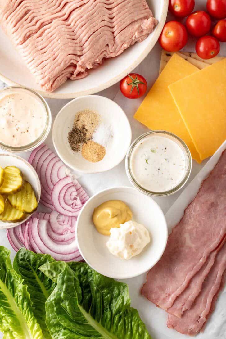 Ground turkey on a plate next to slices of cheese, onion and lettuce.