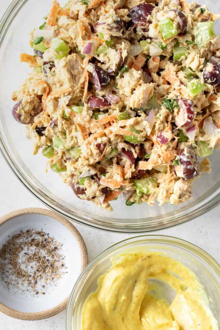 A clear glass bowl filled with canned salmon salad. A small clear bowl has a creamy dressing in it.