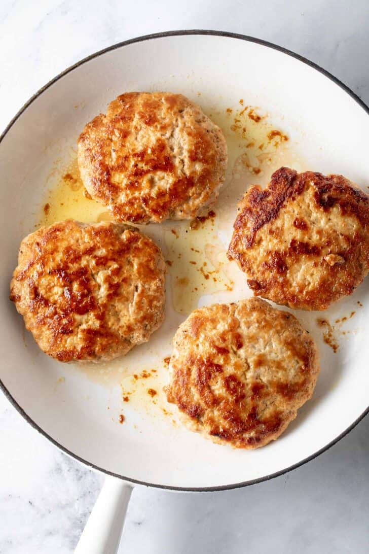 A white skillet filled with 4 cooked turkey burgers.