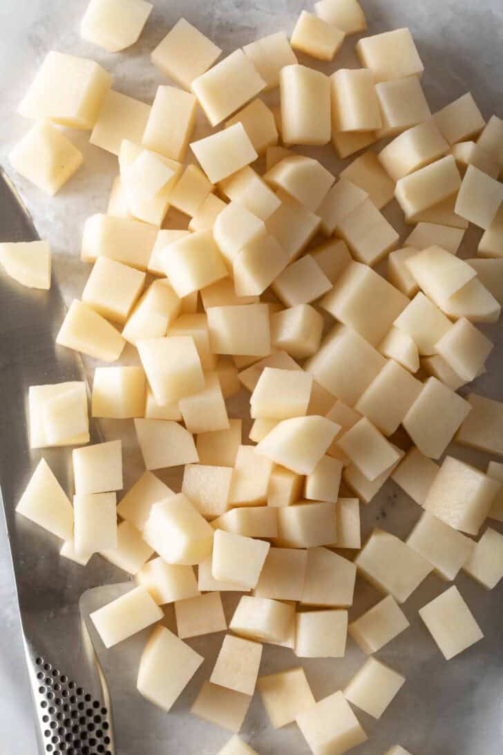 Diced russets on a cutting board with a knife.