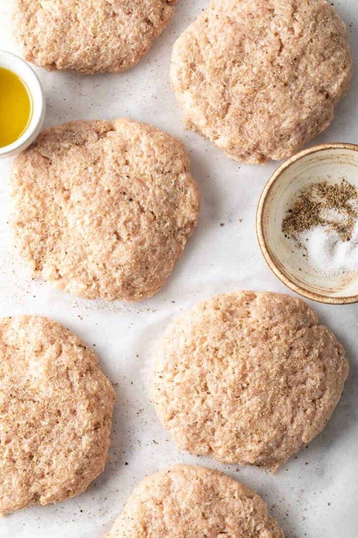 6 raw ground meat burgers on parchment paper.