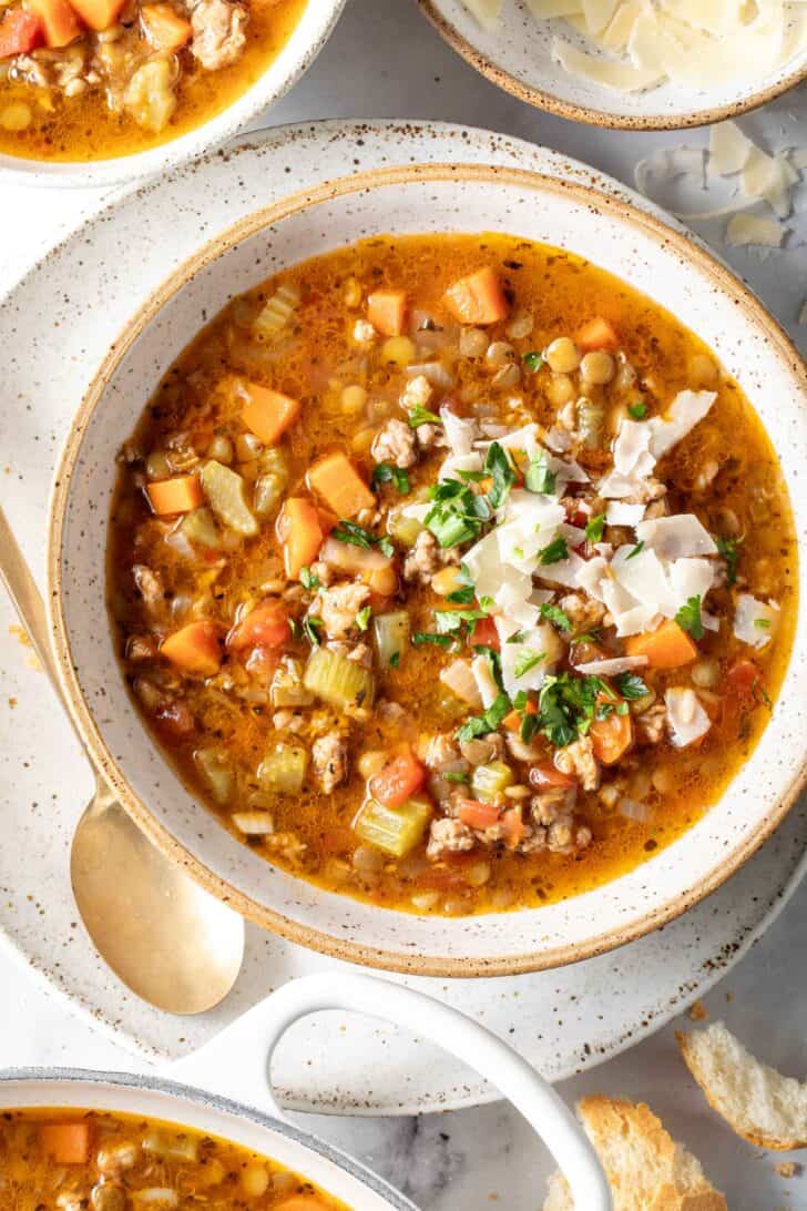 A cream colored bowl filled with broth, vegetables and legumes.