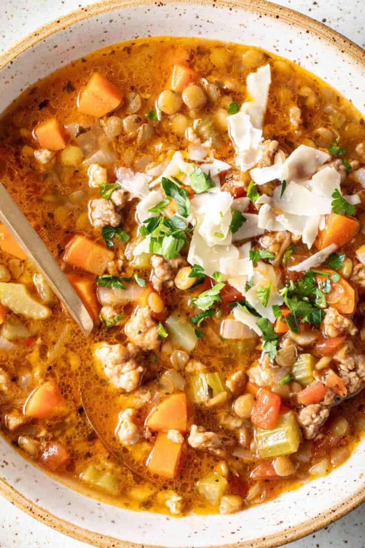 A cream colored bowl filled with Sausage Lentil Soup. A spoon rests in the bowl.