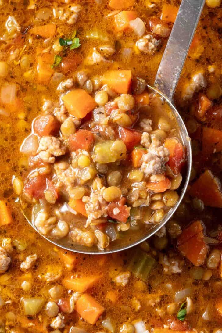 A ladle in a soup bowl filled with Sausage and Lentil Soup.