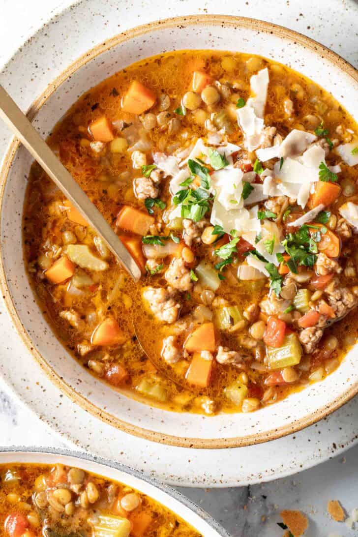 A cream colored bowl filled with Sausage and Lentil Soup.