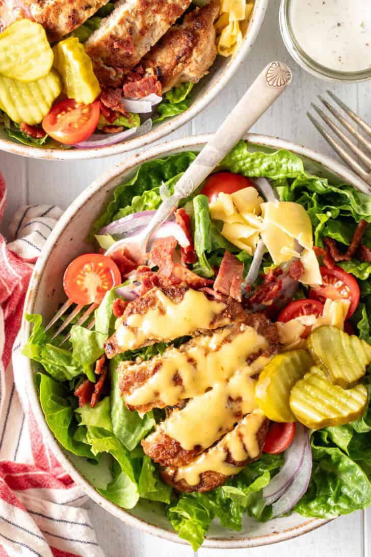 A white bowl filled with turkey patty on top of a salad.