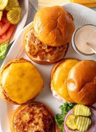 A platter with ground turkey patties and buns on it.