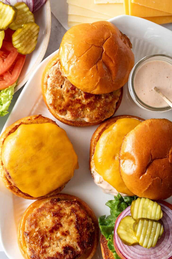 A white platter with 4 ground turkey patties on it.