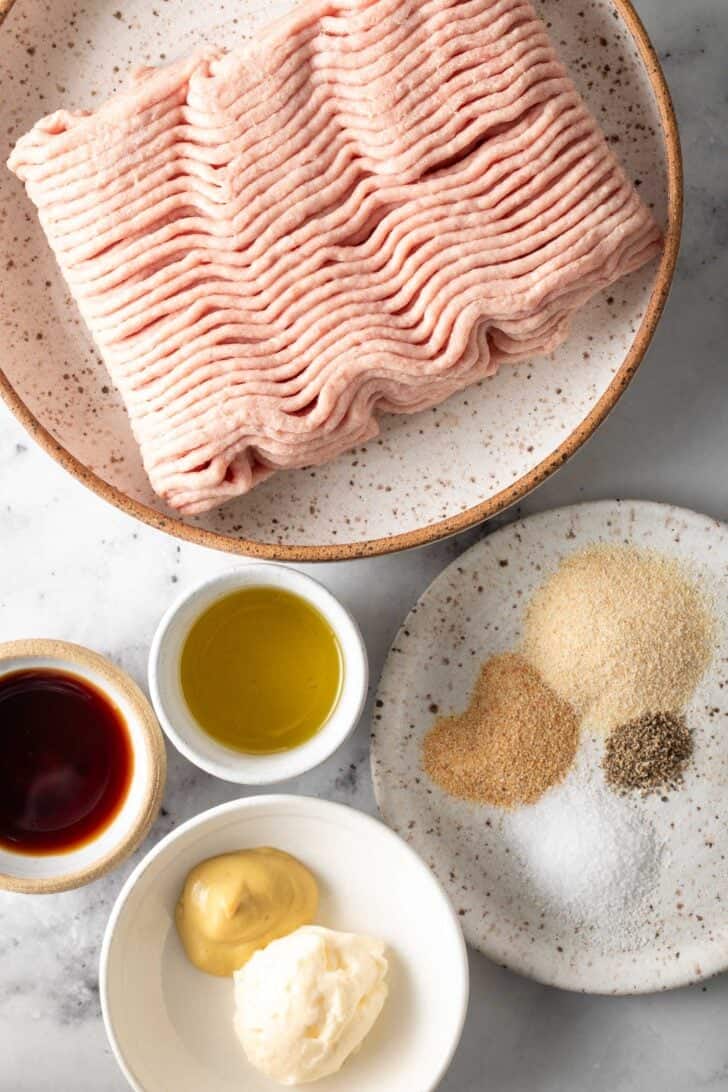 Ground meat on a plate next to a plate with different seasonings on it.