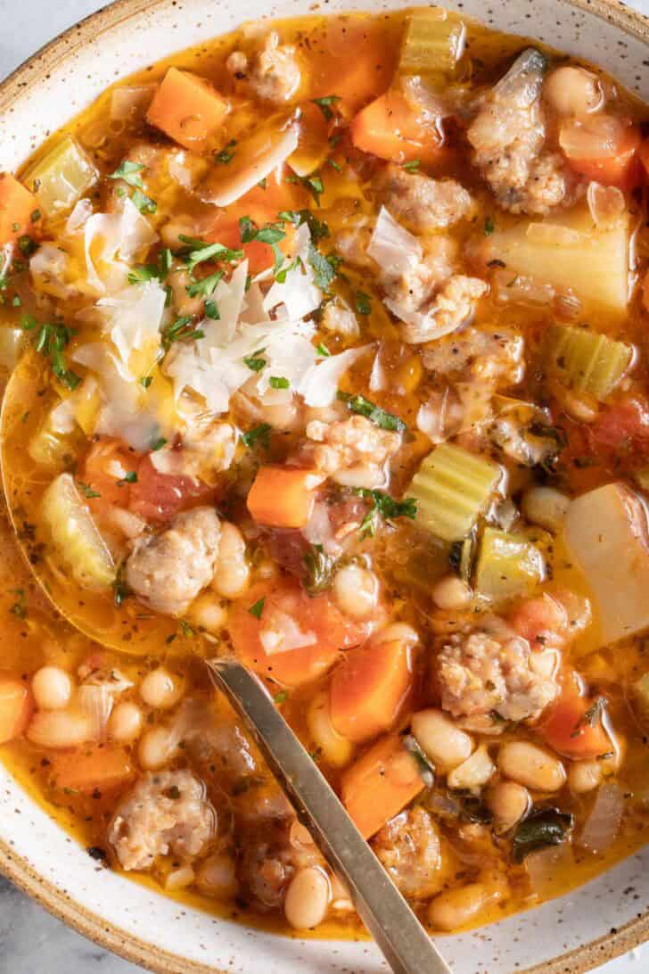 A white bowl filld with Italian Sausage Kale White Bean Soup. A spoon rests in the bowl.