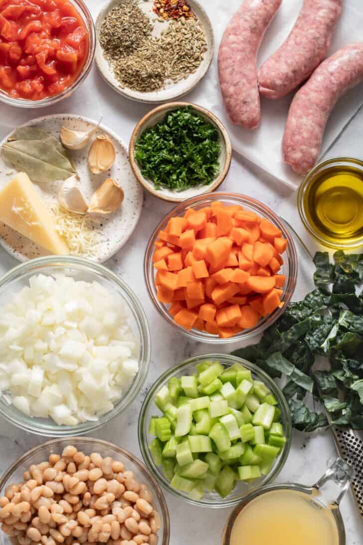 Small glass bowls filled with chopped celery, onion, carrots, parsley and olive oil.